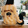 Back view of woman wearing custom dog face pajama in light yellow stripes, sitting with her small black dog