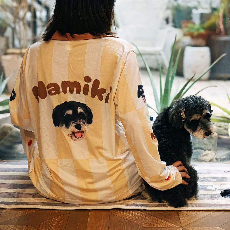 Back view of woman wearing custom dog face pajama in light yellow stripes, sitting with her small black dog